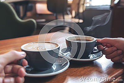 Two people`s hands holding coffee and hot chocolate cups on wooden table in cafe Stock Photo