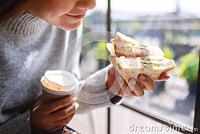 A woman holding and eating whole wheat sandwich and coffee in the morning Stock Photo