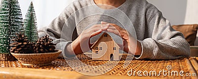 A woman protecting and covering wooden house model by hands with warmness Stock Photo