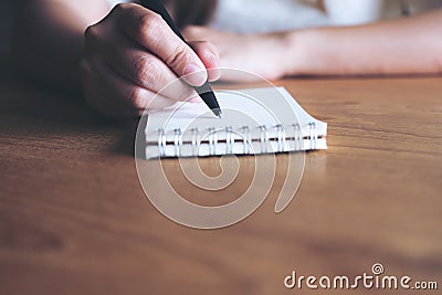 A woman`s hand writing down on a white blank notebook on wooden table Stock Photo