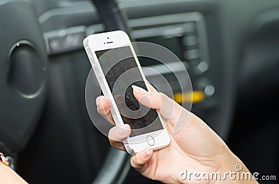 Closeup inside vehicle of hand holding smartphone, steering wheel and black interior background, female driver concept Editorial Stock Photo