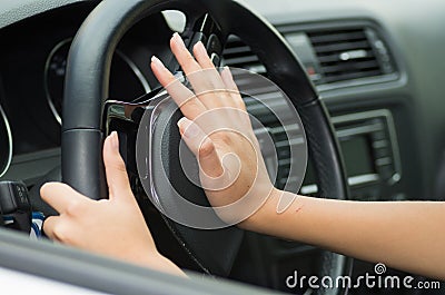 Closeup inside vehicle of hand pushing on steering wheel honking horn, black interior background, female driver concept Stock Photo