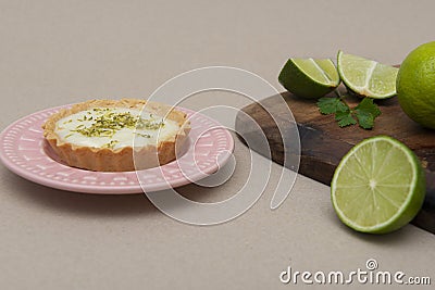 Closeup of a key lime tartlet on a plate with some sliced key limes on a wooden board Stock Photo