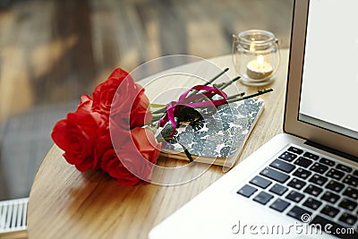 Closeup laptop screen and keyboard on wooden table. Roses red flowers present for St. Valentine`s Day. Stock Photo
