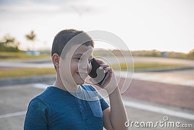 Closeup of a Latino boy talking on the phone with a smile on the street at sunset Stock Photo