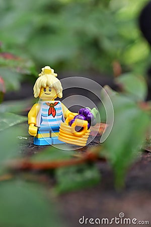 Closeup of a Lego minifigure of a woman with a basket with grapes on a rock Editorial Stock Photo