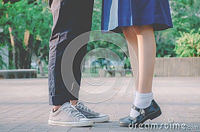 Closeup legs and sneakers of young beautiful couple in school uniform standing on the street in park summer evening, Stock Photo