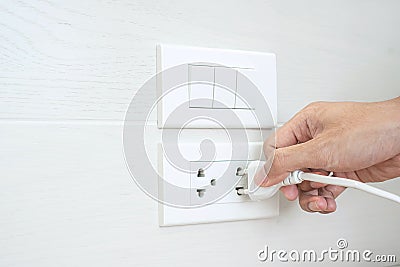 Closeup Male finger unplugging or plugging of electricity device on white wall at home. Energy Saving, power, electrical and Stock Photo