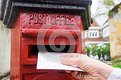 Closeup on a male hand putting a letter in a red letterbox. Concept of vintage type of communication. Stock Photo