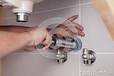 Closeup male plumber's hand fixing sink in bathroom with tile wall. Professional plumbing repair service, installation of water Stock Photo