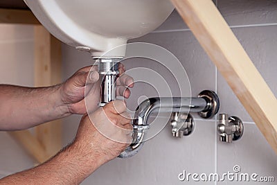 Closeup male plumber worker in blue denim uniform, overalls, fixing sink in bathroom with tile wall. Professional plumbing repair Stock Photo