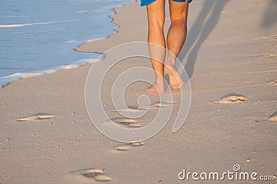 Closeup of a man's bare feet walking at a beach at sunset, with a wave's Stock Photo