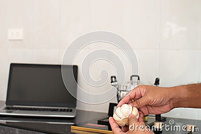 Closeup, A man's hand is holding garlic for home kitchen cooking. In the kitchen there is a pot on the gas stove. Stock Photo