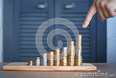 Close-up of a mans hand pointing at columns of multi-colored coins of increasing height, concept of saving and saving money, Stock Photo