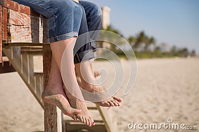 Closeup of man`s and woman`s feet. People sitting on the wooden deck on the beach. Stock Photo