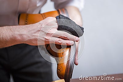 Closeup of Mans Hands with Cleaning Cloth Used for Polishing Tan High Derby Boots. Against Grey Stock Photo