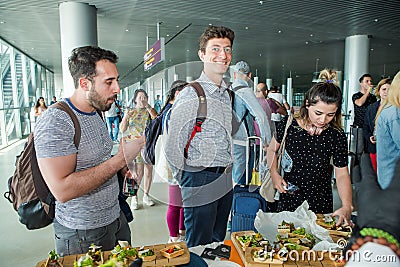 Closeup many passengers try snacks from free degustation table in Lviv airport hall Editorial Stock Photo