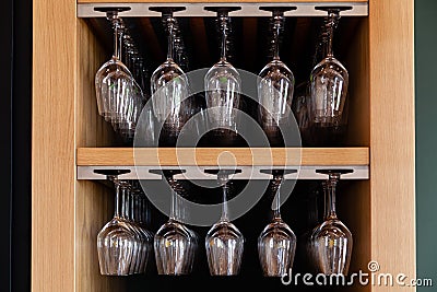 Closeup many upside down empty clear transparent crystal upturned wine glasses hanging in straight row on brown wooden Stock Photo