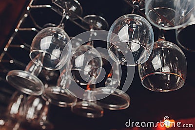 Closeup many upside down empty clear transparent crystal upturned wine glasses hanging in straight rows on brown wooden Stock Photo