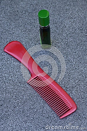 Closeup the maroon color comb with green color gooseberry hair oil over out of focus grey background Stock Photo