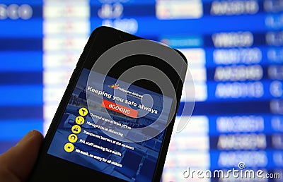 Closeup of mobile phone screen with Philippine airlines booking app, blurred arrival board background Editorial Stock Photo