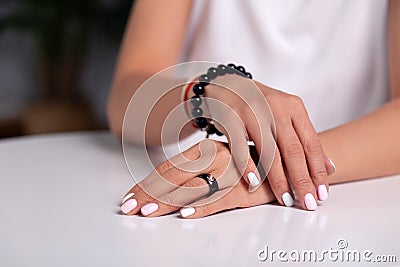 Closeup model hands with manicure, white nails, black ring with stone, bracelet made of shiny black beads, red, beige braided Stock Photo