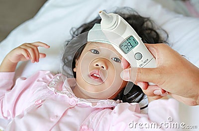 Closeup mother hand takes temperature for her daughter with high pressure of ear thermometer on bed at home Stock Photo