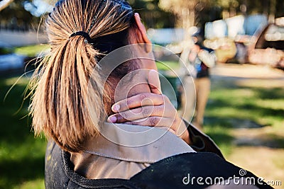 Closeup, neck pain and hand of woman with injury in paintball, sports and training on blurred background. Rear view Stock Photo