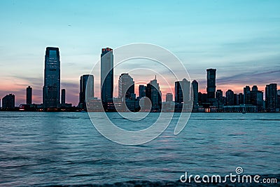 Closeup of New Jersey cityscape at sunrise with skyscrapers silhouettes and a sea reflecting colors Stock Photo