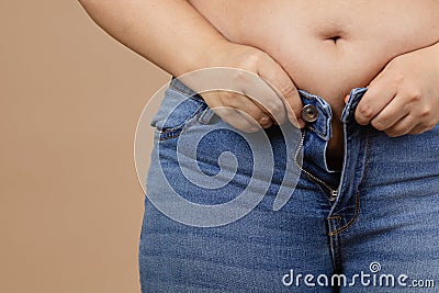 Closeup of obese woman with overweighted stomach zipping up jeans. Sudden weight gain. Visceral fat. Body positive Stock Photo