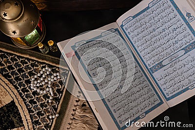 Closeup of open Quran book with rosary beads, praying mat an lantern in background. Stock Photo