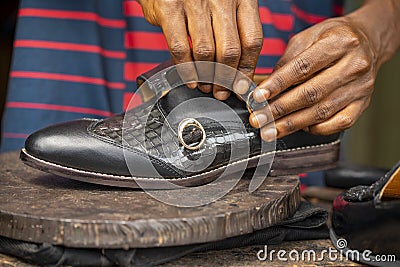 Closeup of a pair of hands fixing a black shoe on a wooden surface Stock Photo