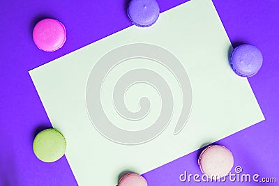 Closeup paper for copy space, text and advertising on purple background with multicolored pink and yellow macaroons Stock Photo