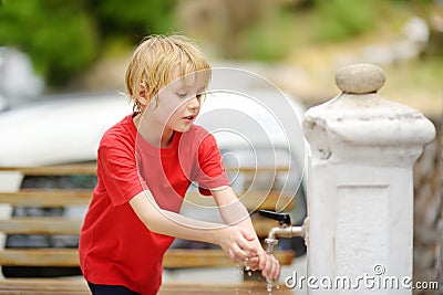 Closeup photo of child washing hands in a city fountain. Little boy drinking clean water from a street pump Stock Photo