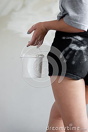 A closeup photo of a girl soiled with white putty holding a bucket against a background of plaster walls. Stock Photo