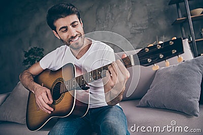 Closeup photo of mixed race guy sitting sofa hold acoustic instrumental guitar playing new written song sound love his Stock Photo