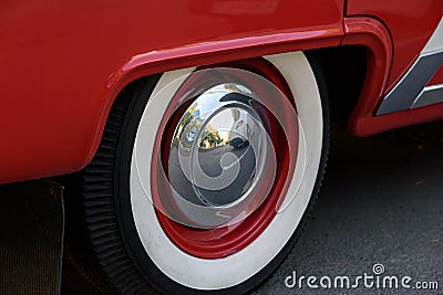 Closeup photo of the rear wheel of a magnificent retro car. The wheel has a red stamped disc in the body color, a large chrome Stock Photo