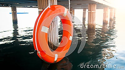 Closeup photo of red saving ring hanging wooden pier. Safety on sea water Stock Photo