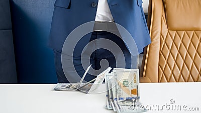 Closeup image of stack of money lying on office desk in front of businessman in blue suit Stock Photo