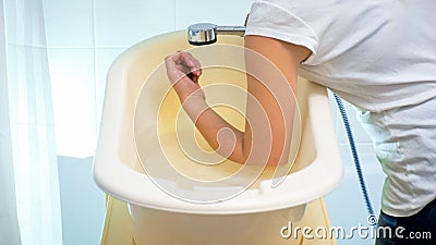 Closeup photo of young woman checking water temperature in baby bathtub with elbow Stock Photo