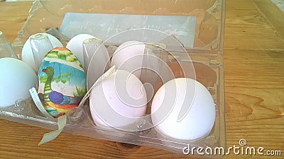 A closeup photograph of a single painted plastic Easter egg nested inside of a plastic egg carton with several real chicken eggs Stock Photo