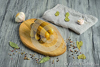 Closeup of pickles on a wooden board with garlic, bay leaves, and peppercorns. Stock Photo