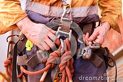 Closeup picture of male rope access worker hand wearing full safety harness clipping carabiner on a chair into harness loop Stock Photo