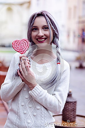 Closeup portrait amazing girl in the white warm woolen sweater with gray silver hair with red and white lollipop Stock Photo