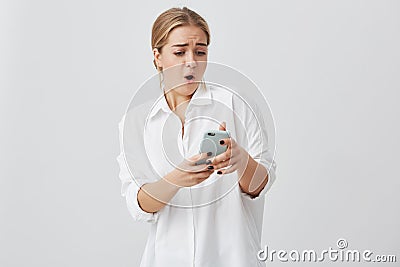 Closeup portrait anxious or shocked young female caucasian with blonde hair looking at phone seeing bad news or photos Stock Photo