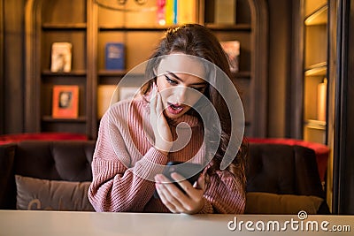 Closeup portrait anxious young girl looking at phone seeing bad news or photos with disgusting emotion on her face cafe background Stock Photo