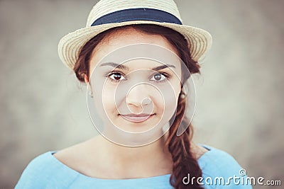 Closeup portrait of beautiful smiling white Caucasian brunette girl with brown eyes and plait, in blue dress and straw hat Stock Photo