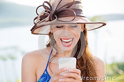 Closeup portrait happy excited young girl in hat looking at phone with toothy smile laugh seeing funny news photos isolated Stock Photo