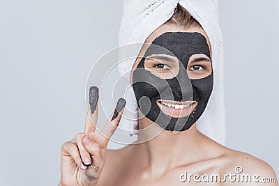 Closeup portrait of happy smiling young woman with cosmetic black clay organic mask on her face, wears black white on hair. Female Stock Photo