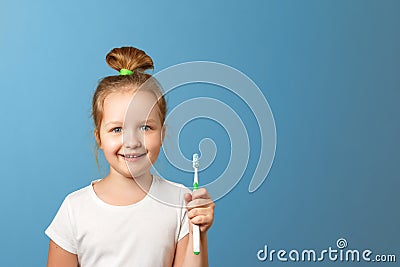 Closeup portrait of a little girl on a blue background. A child holds a toothbrush. The concept of daily hygiene. Stock Photo
